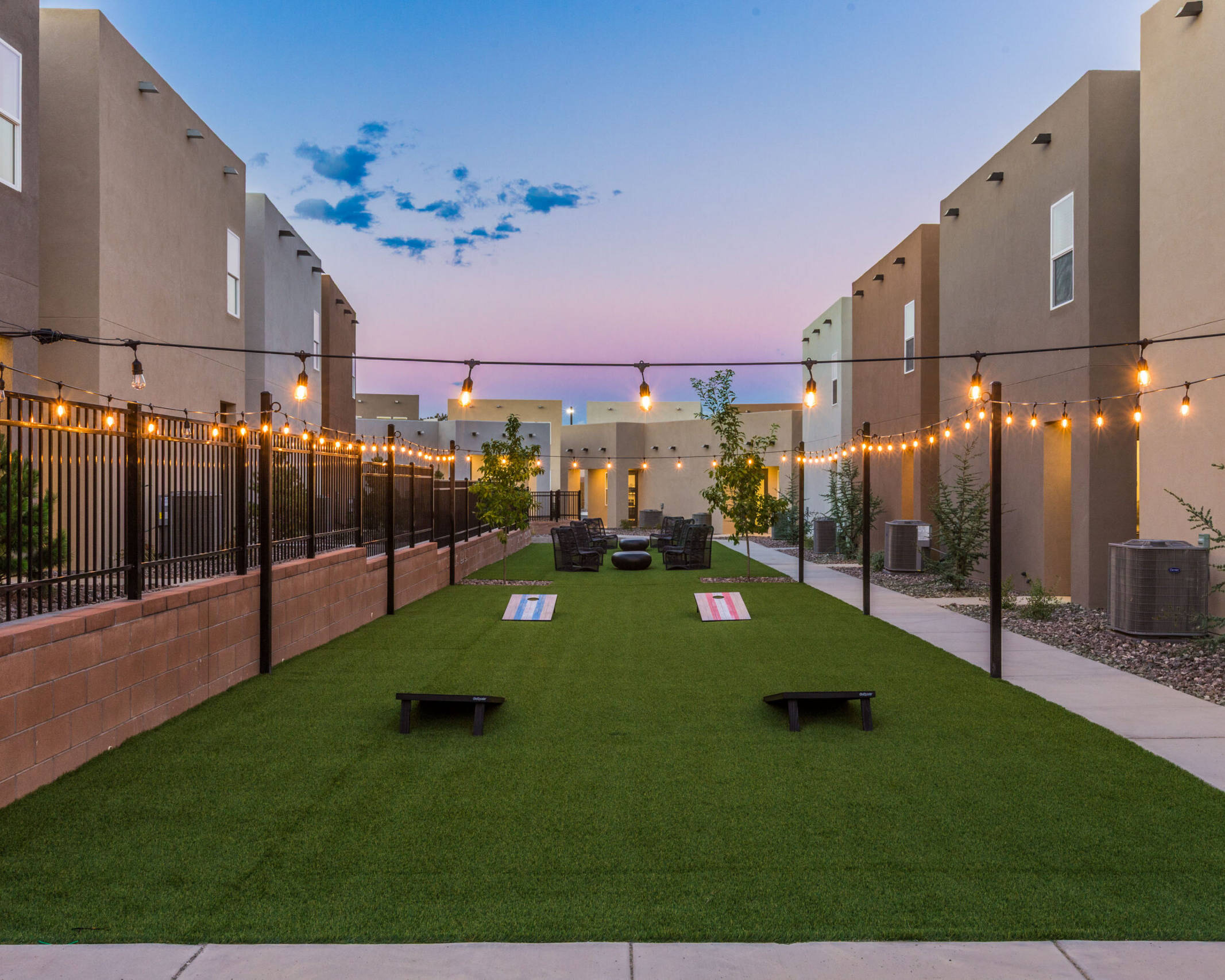 cornhole game boards on turf lawn under warm bulb lights during twilight